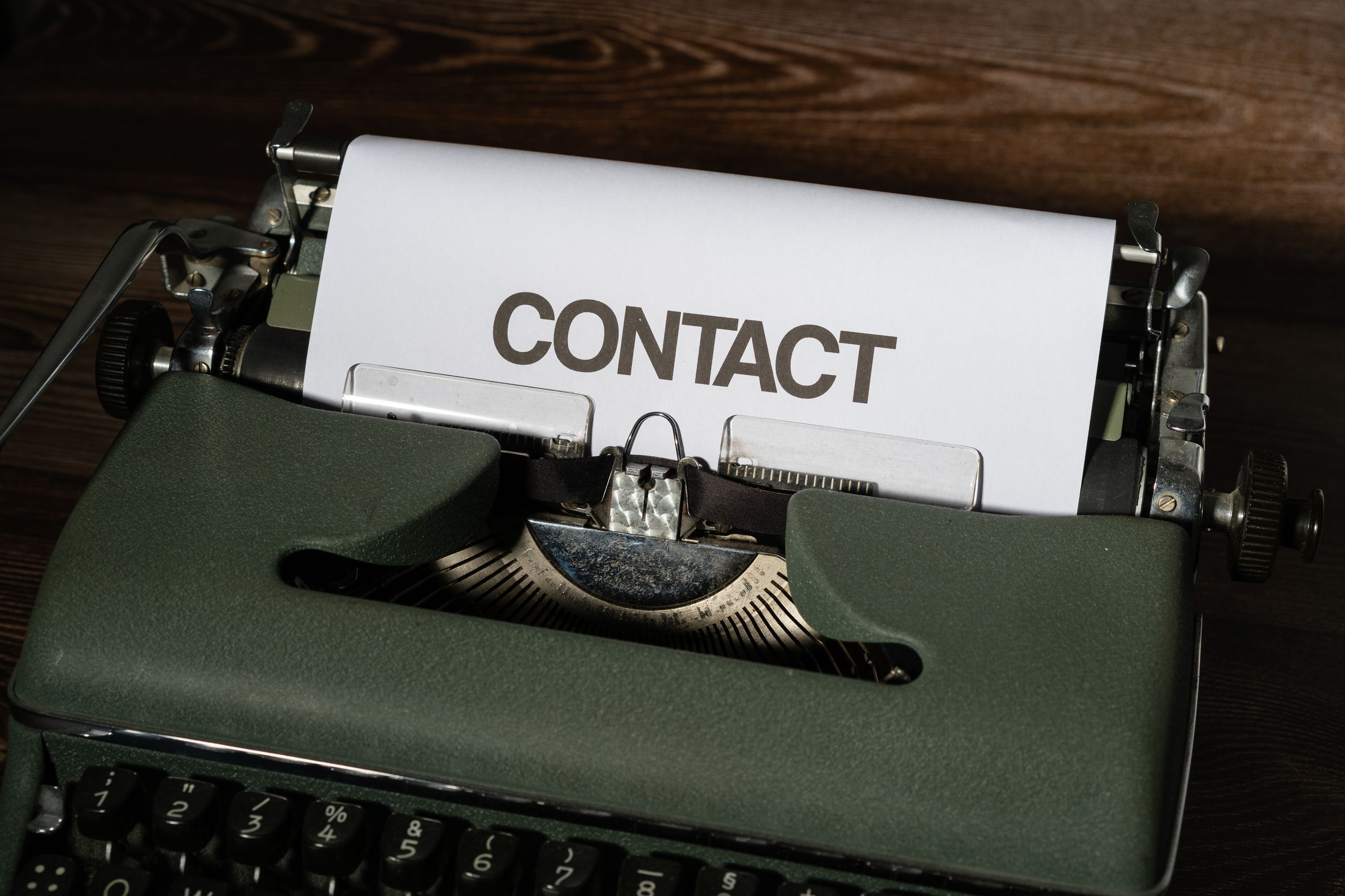 Close-up of a vintage typewriter with a white paper sheet displaying the word 'CONTACT' in bold text.